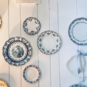 May include: A collection of nine decorative plates with blue and white floral patterns, displayed on a white wall. The plates are various sizes and shapes, with some featuring a raised rim.