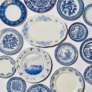 May include: A collection of blue and white ceramic plates with various designs, including floral patterns, dragons, and ships. The plates are arranged on a white background.