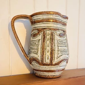 Peut inclure: Un pichet en céramique blanche avec des motifs géométriques bruns et verts. Le pichet a une large ouverture et une anse.