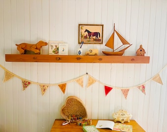 Peut inclure: Une étagère en bois avec divers objets décoratifs, dont un voilier en bois, un chien en jouet, une image de chevaux et deux livres. Il y a aussi une petite maison en bois et une guirlande de drapeaux en tissu suspendue sous l'étagère.