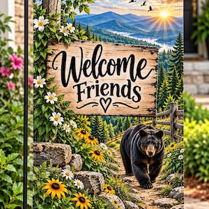 May include: A rectangular garden flag featuring a wooden sign with the text Welcome Friends and a heart symbol. The scene depicts a black bear walking on a dirt path through a forest with yellow flowers, green foliage, and a mountain sunrise.