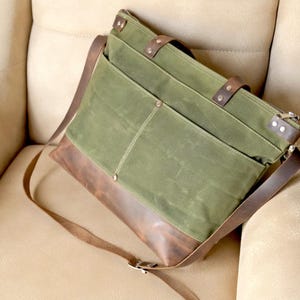 May include: A green and brown canvas and leather tote bag with a long shoulder strap. The bag has multiple pockets and a zipper closure.