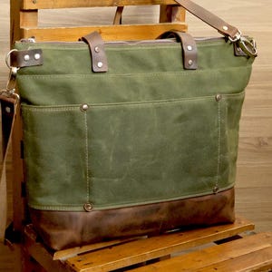 May include: A green canvas tote bag with brown leather accents and a zipper closure. The bag has a long shoulder strap and two top handles.