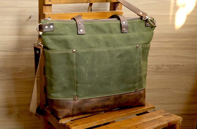 May include: A green canvas tote bag with brown leather accents and a zipper closure. The bag has a long shoulder strap and two top handles.