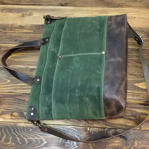 May include: A green canvas tote bag with brown leather accents and a long brown leather strap. The bag has a zipper closure and multiple pockets.