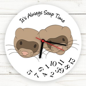 May include: White round wall clock featuring two cartoon ferrets. The clock face has black numbers and hands, with a red second hand. The text "It's Always Soup Time" is printed above the ferrets.