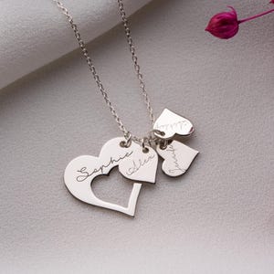 May include: A silver necklace with a chain and multiple heart-shaped pendants. The largest heart has a cutout and the name "Sophie" engraved. Smaller hearts are engraved with the names "Alex" and "Jennifer" and "Ashley".
