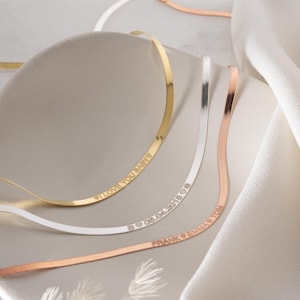 Könnte beinhalten: Nahaufnahme von drei zarten Halsketten in Gold, Silber und Roségold. Die goldene Halskette trägt die Inschrift "I LOVE YOU BABY". Die silberne Halskette trägt die Inschrift "06.04.2018". Die roségoldene Halskette trägt die Inschrift "FRANK & EMMA".
