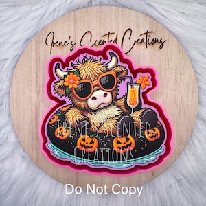 May include: A round wooden sign featuring a cartoon Highland cow wearing sunglasses and a flower, floating in a pool float with jack-o'-lanterns. The sign has the text "Irene's Scented Creations" and "Do Not Copy".