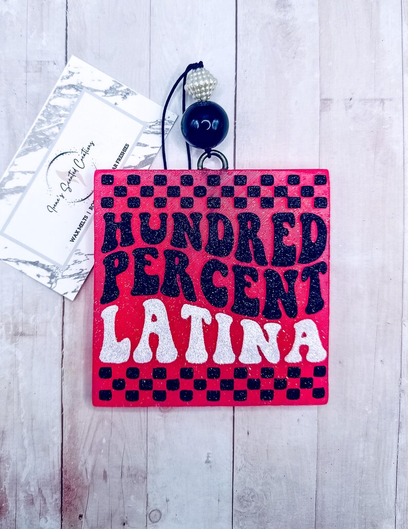 May include: A pink wooden sign with black and white checkered border. The sign says "HUNDRED PERCENT LATINA" in black and white glitter letters.