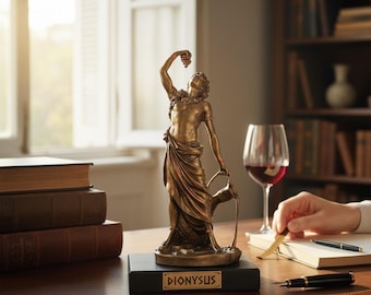 Può includere: Una statua color bronzo della figura di Dioniso su una base rettangolare nera con il nome DIONYSUS stampato su una targhetta dorata. La figura tiene un grappolo d'uva sopra la testa e versa del liquido da un recipiente in un contenitore.