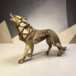 May include: A gold-colored wolf figurine featuring a geometric, faceted design. The wolf is depicted in a standing position with its head tilted upward as if howling. The surface has a distressed, metallic finish with dark brown accents.