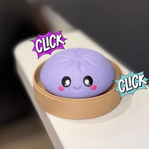 May include: A 3D-printed, lavender-colored dumpling with a smiling face and pink cheeks sits in a tan steamer basket. The word "CLICK" is in a comic book style speech bubble.