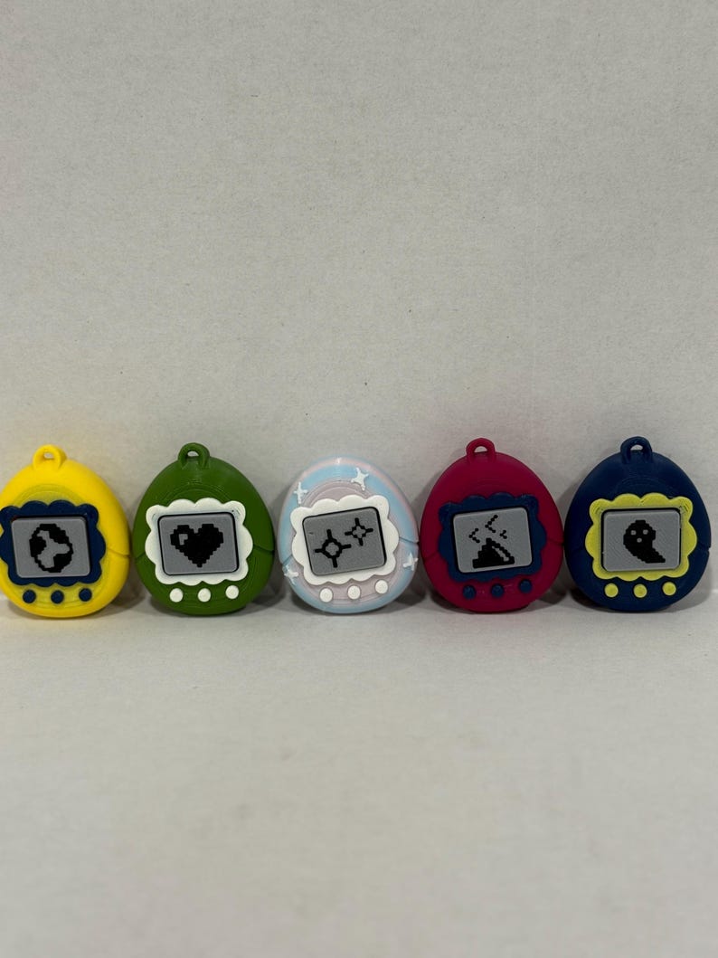 May include: Five colourful, egg-shaped digital pet toys. Each has a different colour shell: yellow, green, light blue, red, and dark blue. The screens display pixelated graphics of a globe, heart, astrological symbols, volcano, and ghost.