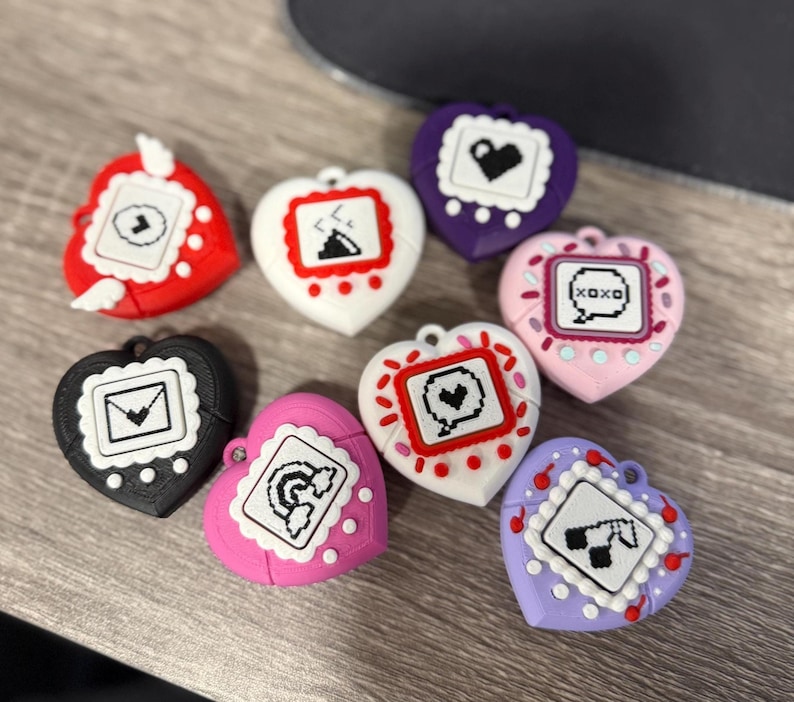 May include: A collection of heart-shaped accessories in various colors, including red, white, black, pink, and purple. Each accessory features a pixelated design within a white border. The accessories are arranged on a wooden surface.
