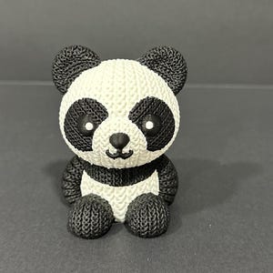 May include: A small, white and black knitted panda bear figurine. The panda has black eyes and a black nose.