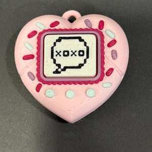May include: A pink heart-shaped pendant with a rectangular center displaying the text "XOXO" in a speech bubble. The pendant is decorated with sprinkles and small circles.