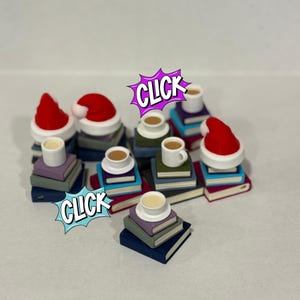 Pode incluir: Miniaturas de pilhas de livros cobertas com pequenas chávenas de café e gorros de Pai Natal. A imagem inclui a palavra "CLICK" numa bolha de banda desenhada. Os livros são de várias cores, incluindo azul, roxo e vermelho.