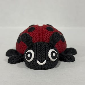 May include: A red and black knitted ladybug toy with white eyes and a smiling mouth.