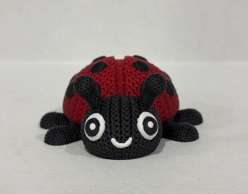 May include: A red and black knitted ladybug toy with white eyes and a smiling mouth.