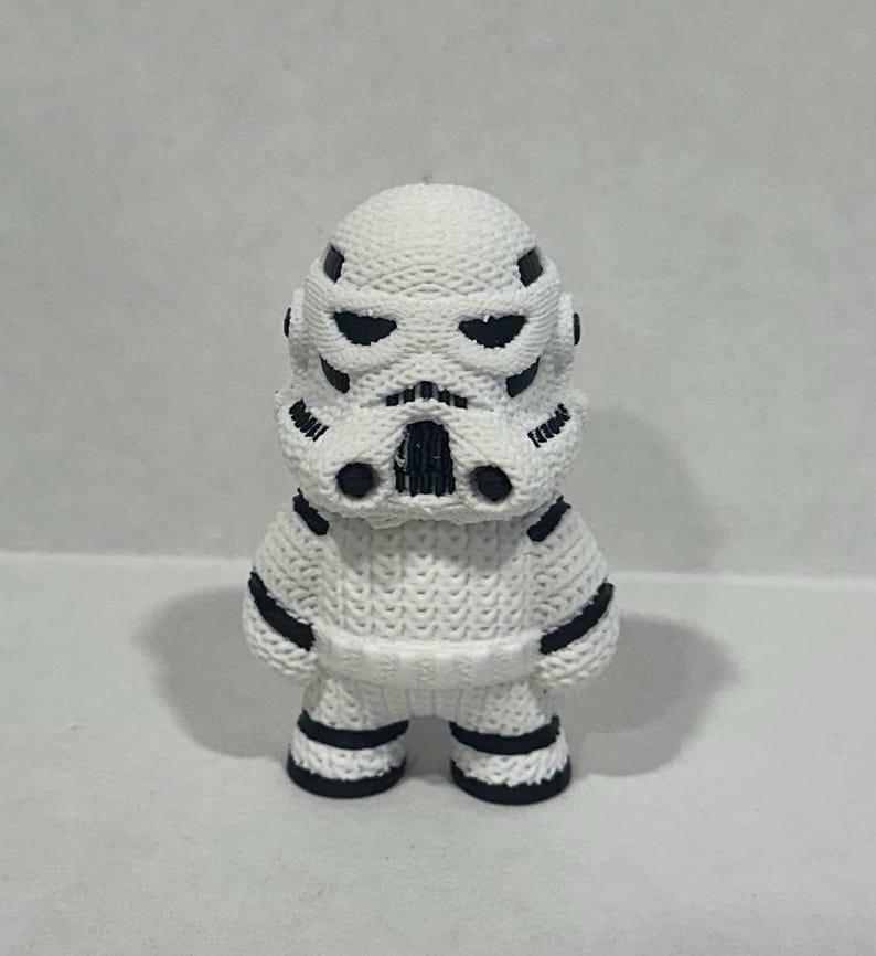 May include: A white and black stormtrooper figurine with a knitted texture. The figurine has a black face mask and black details on the body.
