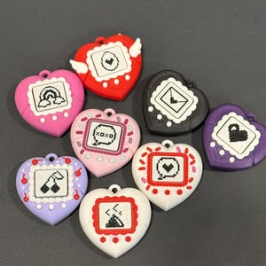 May include: A collection of heart-shaped, colorful accessories with pixelated designs. Each heart features a different graphic, including a rainbow, cherries, and the text "XOXO". The accessories are in various colors, such as red, pink, purple, black, and white.