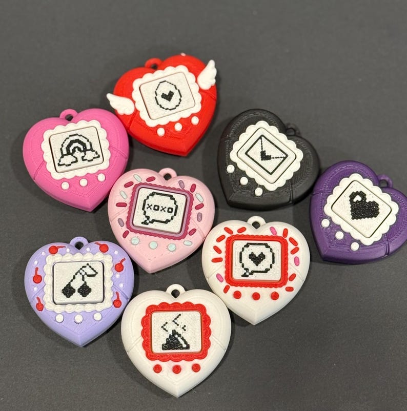 May include: A collection of heart-shaped, colorful accessories with pixelated designs. Each heart features a different graphic, including a rainbow, cherries, and the text "XOXO". The accessories are in various colors, such as red, pink, purple, black, and white.