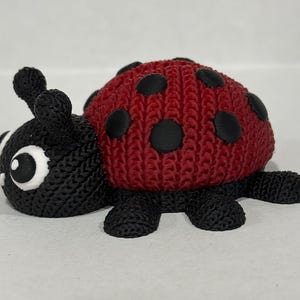 May include: A red and black ladybug toy with a knitted texture. The ladybug has black spots and a black head with white eyes.