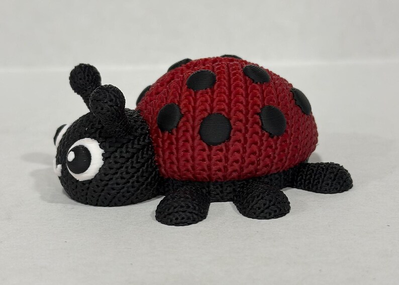 May include: A red and black ladybug toy with a knitted texture. The ladybug has black spots and a black head with white eyes.
