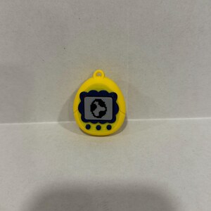 May include: Yellow handheld digital pet toy with a blue and black screen. The toy has a small loop at the top for attaching to a keyring. Three small yellow buttons are located below the screen.
