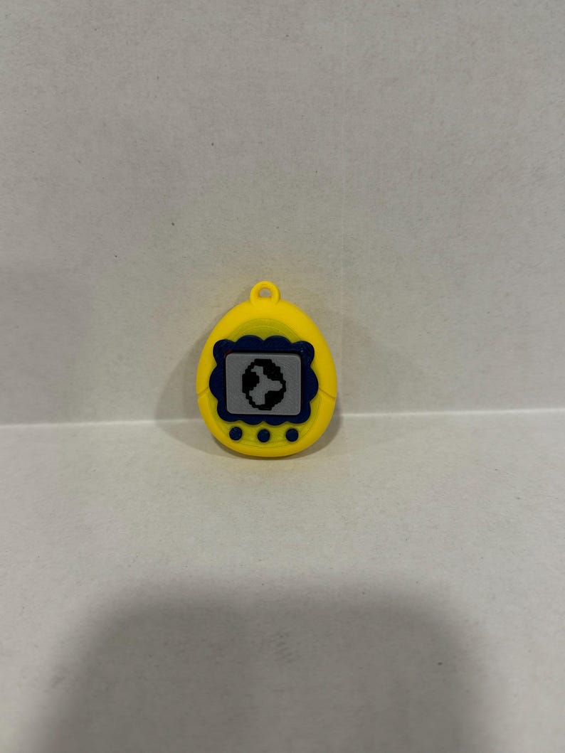 May include: Yellow handheld digital pet toy with a blue and black screen. The toy has a small loop at the top for attaching to a keyring. Three small yellow buttons are located below the screen.