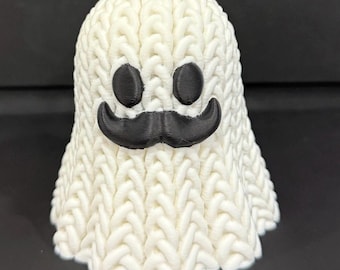 May include: A 3D-printed white ghost figure with a knitted texture. It features a black moustache and two black oval eyes. This whimsical figure is a decorative item.