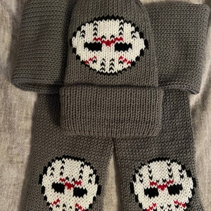 May include: Gray knitted hat and scarf set with a white and red embroidered hockey mask design.