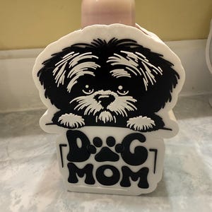 May include: A white and black Shih Tzu dog-themed soap dispenser with the words "DOG MOM" in black. The dispenser has a cute dog face design and paw prints.