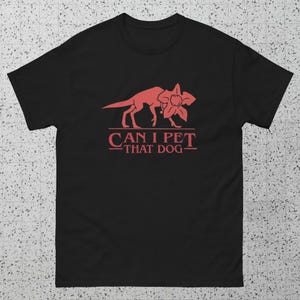May include: Black t-shirt with a red graphic of a dog and flower, and the text "CAN I PET THAT DOG". The design is centered on the front of the shirt. The shirt is made of a soft material.
