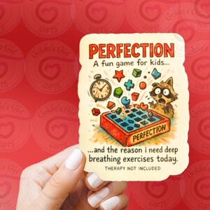 May include: A rectangular card with the word "PERFECTION" in red letters. The card features a cartoon raccoon, a clock, and various game pieces. Text on the card reads "A fun game for kids..." and "...and the reason I need deep breathing exercises today."