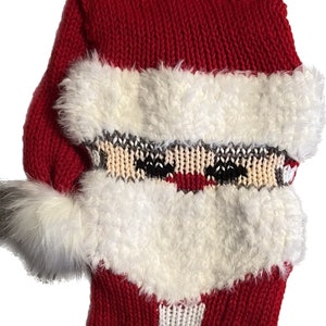 May include: Red and white knitted Santa stocking with a white fur trim and a white pom-pom on the top. The stocking has a loop for hanging and a fringe at the bottom.