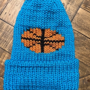 May include: A blue knitted beanie with an orange and black basketball design.