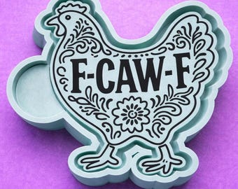 May include: A light blue chicken-shaped cookie cutter featuring a black decorative floral pattern and the text F-CAW-F printed across the center. The object has a raised edge and a smooth finish, designed for cutting dough into a specific shape.