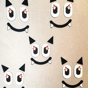 May include: Five black felt cutouts of a cartoon monster face with white eyes and red flames. The monster has a wide smile with two fangs on each side.