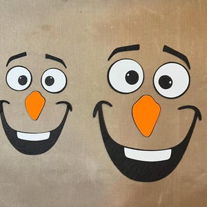 May include: Two felt snowman faces, one larger than the other, with black eyes, mouths, and eyebrows, and orange felt noses.