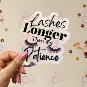 May include: A white sticker with the text "Lashes Longer Than my Patience" in black script and a pair of false eyelashes. The sticker is held against a background of gold sequins.