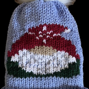 May include: A blue knitted winter hat with a white pom pom on top. The hat has a red, white, and green knitted design on the front. The hat has a brown leather tag with the text "Cuddles & Chill" on it.