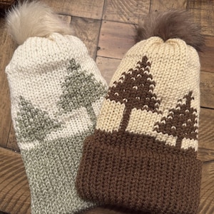 May include: Two knitted winter hats with pom poms. One hat is white with brown trees and a brown brim. The other hat is white with green trees and a green brim.