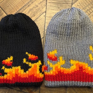 May include: Two knitted hats with a flame design. One hat is black with orange and red flames, and the other is grey with yellow, orange, and red flames.