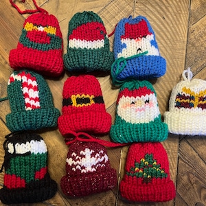 May include: Twelve knitted Christmas ornaments in the shape of Santa hats. The ornaments are decorated with various Christmas themes, including candy canes, snowmen, and Christmas trees.