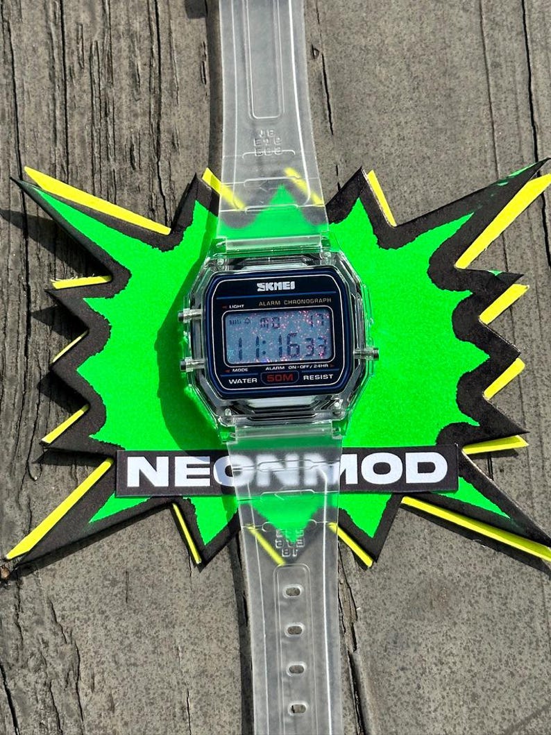 May include: A digital wristwatch with a clear, transparent plastic strap and a rectangular case. The watch face features a black background with the text SKMEI, ALARM CHRONOGRAPH, and WATER 50M RESIST. The digital display shows the time 11:16:33.