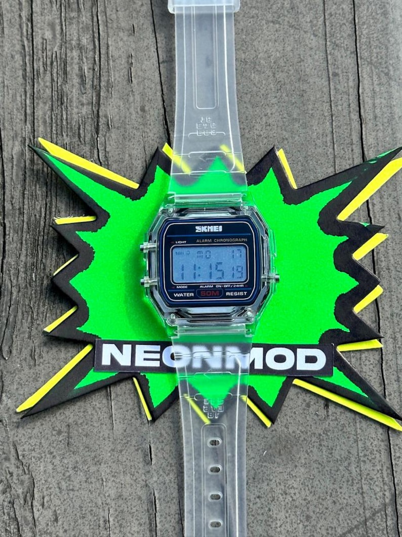 May include: A digital wristwatch with a clear, transparent plastic strap and case. The watch face features a black border with the text SKMEI, ALARM CHRONOGRAPH, and WATER 50M RESIST. The digital display shows the time 11:15 and the date MO 17.