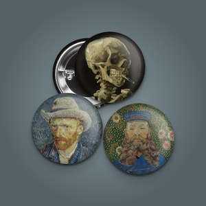 May include: Three round pinback buttons featuring artwork. One button displays a skull smoking a cigarette on a black background. Another depicts a portrait of Vincent van Gogh. The third button shows a portrait of a man with a beard.