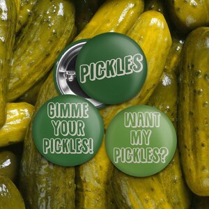 Può includere: Tre bottoni rotondi verdi con testo bianco. I bottoni dicono "PICKLES", "GIMME YOUR PICKLES!" e "WANT MY PICKLES?" su uno sfondo di sottaceti gialli.